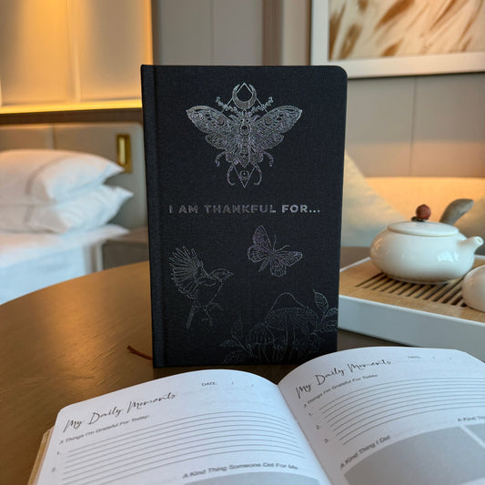 Black notebook with butterfly designs on a table with an open book in front