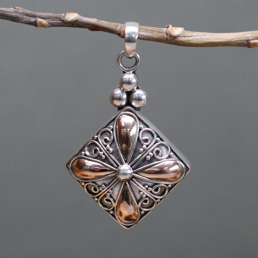 Silver pendant with intricate designs hanging from a branch against a gray background